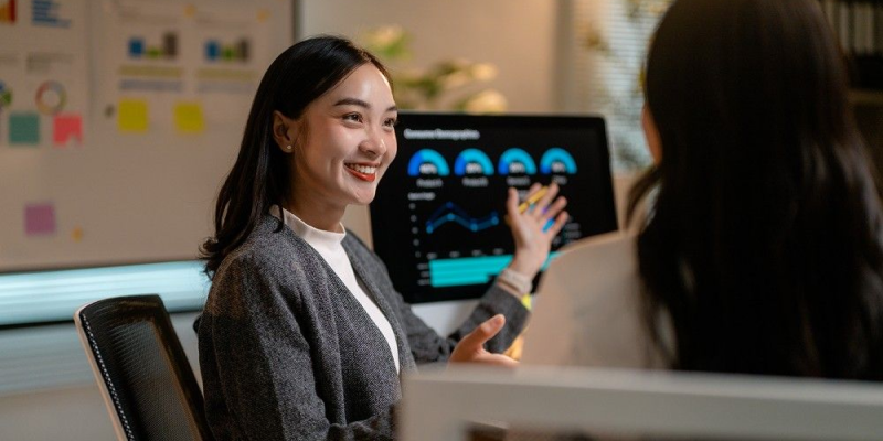 Profissional de vendas apresentando gráficos de desempenho no CRM para uma colega em ambiente corporativo.