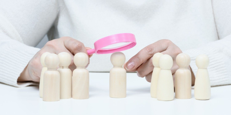 Pessoa usando lupa para destacar um boneco de madeira entre vários.